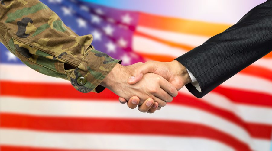 American soldier in uniform and civil man in suit shaking hands with adequate national flag on background